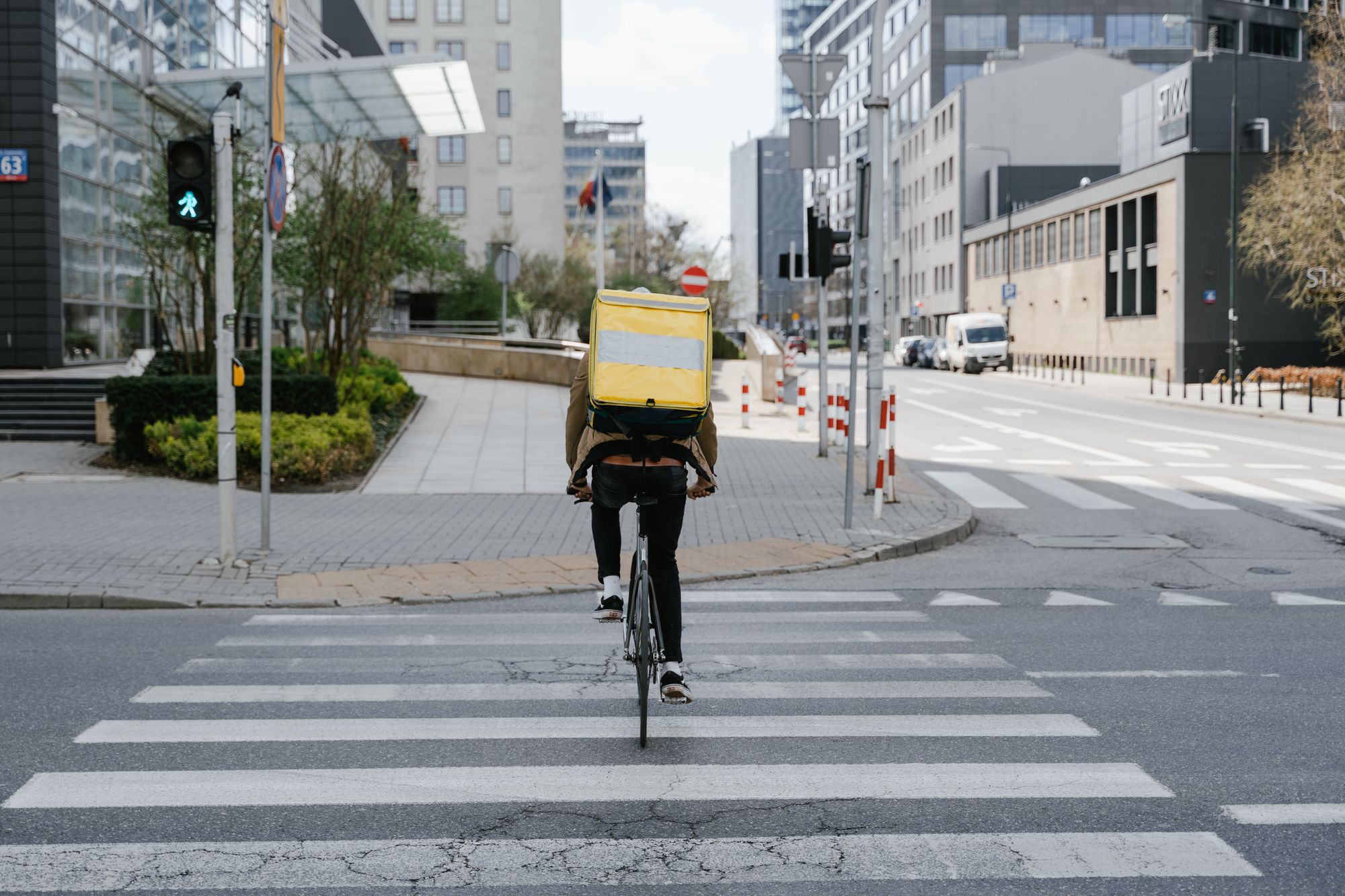 Cyclist with thermal bag crossing street in downtown Warsaw, Poland.
