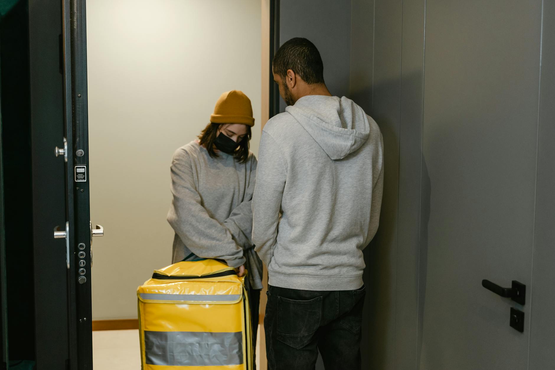 A delivery person hands over a package at an apartment door inside a building.