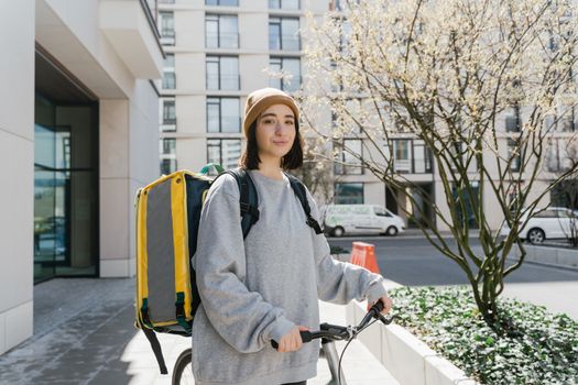 Young woman cyclist with a delivery backpack on a city street ready for food delivery.