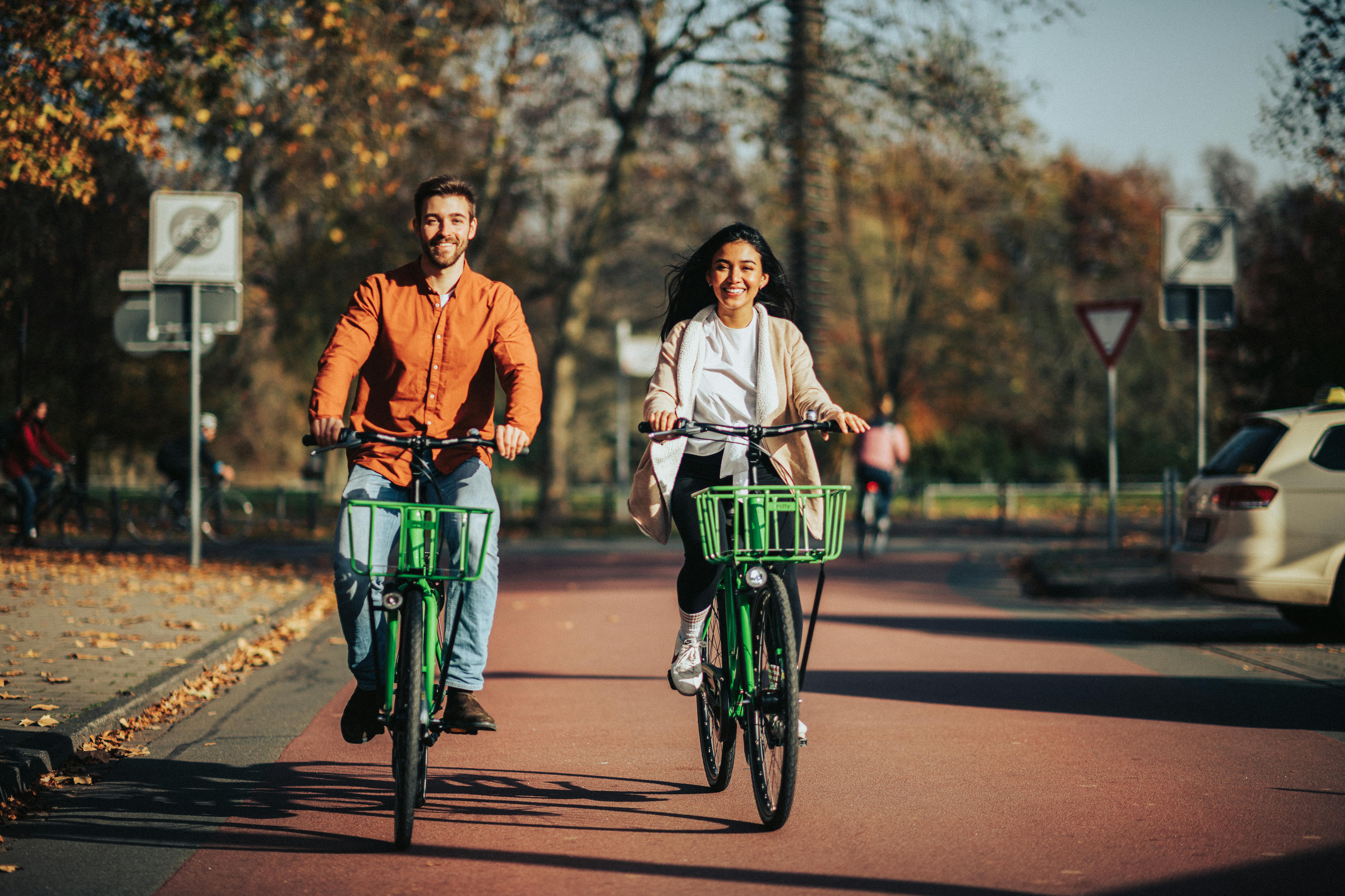 Man and woman riding bicycles on a sunny autumn street in a park.