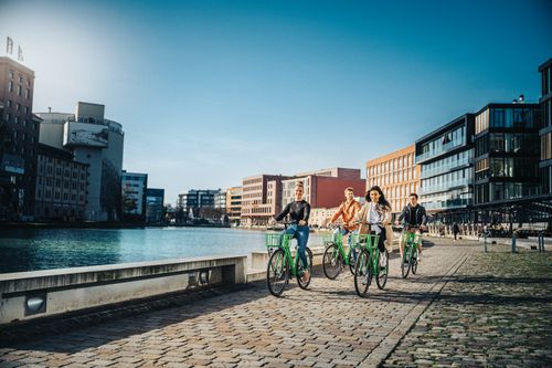 Free People biking along a canal in a modern urban area under a clear sky. Stock Photo