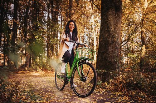 Free A smiling woman rides a green bicycle along a forest trail in autumn. Stock Photo