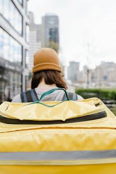 Back view of a courier in a beanie with a thermal bag delivering food in an urban area.
