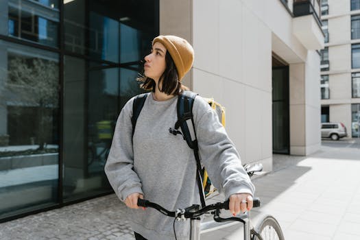 A woman in a beanie rides a bicycle for food delivery service in city streets.