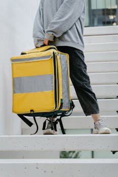 Person carrying a large yellow thermal delivery bag down a modern staircase, ideal for delivery service concepts.