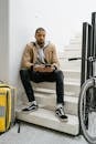 Man in Brown Zip Up Jacket and Black Pants Sitting on the Staircase
