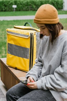 Young woman courier taking a break outdoors with a yellow delivery bag.