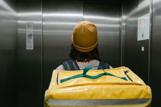 Back view of a delivery person with a yellow thermal bag inside an elevator.