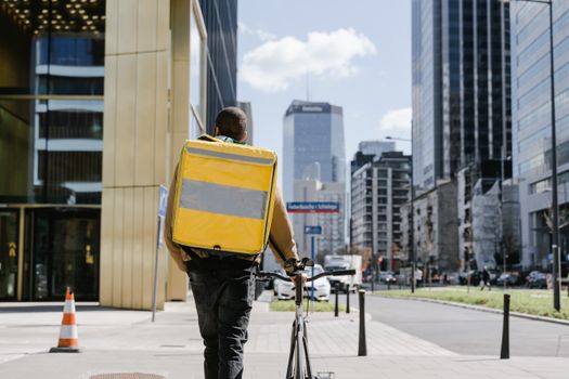 Bicycle courier with large yellow thermal bag delivering food in Warsaw downtown.