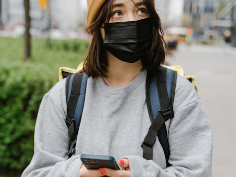 A woman wearing a face mask checks her phone while outdoors in the city.