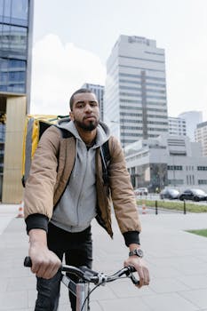 Courier on a bicycle delivering food in an urban city with skyscrapers in the background.