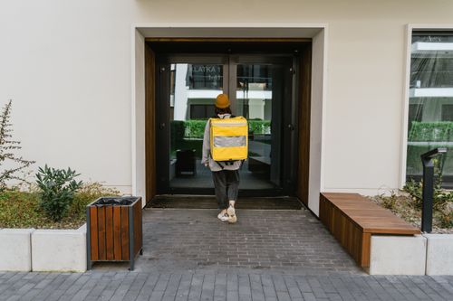 Free A delivery person with a yellow thermal bag approaches a customer's door in a city setting. Stock Photo