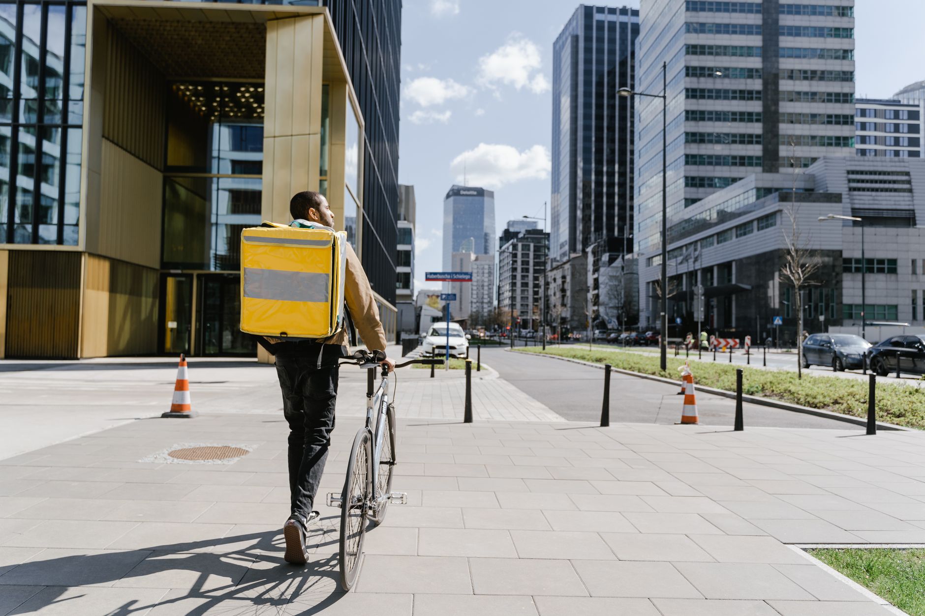 Courier cycling through city street with delivery bag, urban logistics theme.