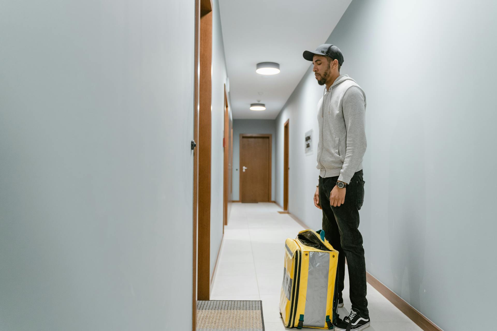 Delivery courier standing in a residential hallway with a yellow bag, waiting to deliver a package.