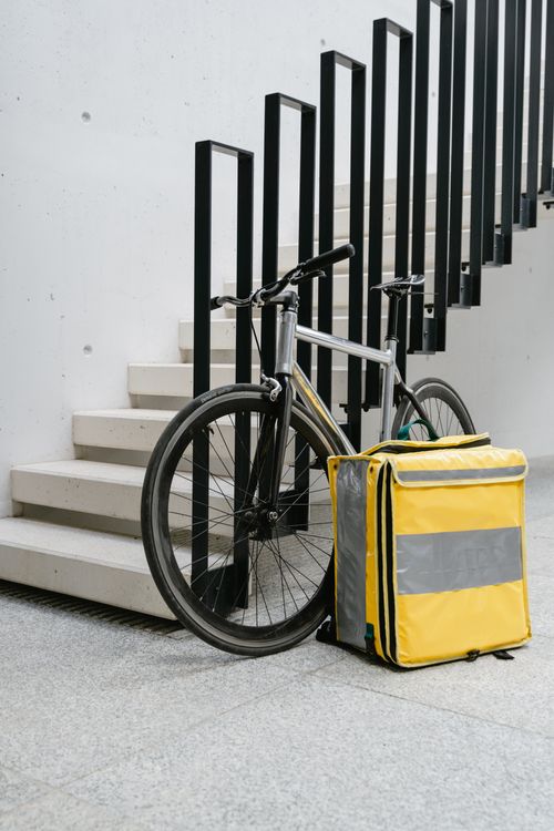 Free Bicycle with a yellow thermal delivery bag parked by indoor stairs, urban setting. Stock Photo