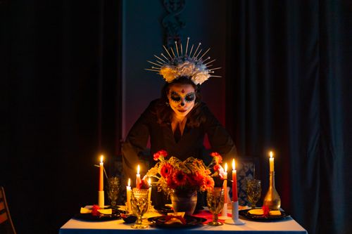 Free A woman with Day of the Dead makeup stands over a candlelit altar. Stock Photo