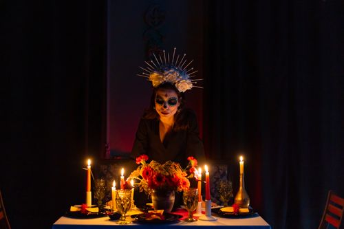 Free A woman with face paint for Día de los Muertos stands by a candlelit table, evoking tradition and mystery. Stock Photo