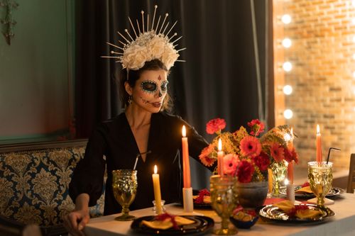 Free A woman with Dia de los Muertos makeup sits at a candlelit table adorned with floral decorations. Stock Photo