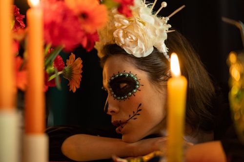 Free A woman in Day of the Dead makeup with flowers and candles creates a vibrant, festive atmosphere. Stock Photo