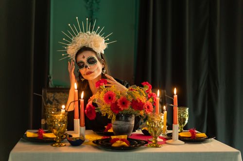 Free Elegant Dia de los Muertos scene featuring a woman with traditional makeup and vibrant table setting. Stock Photo