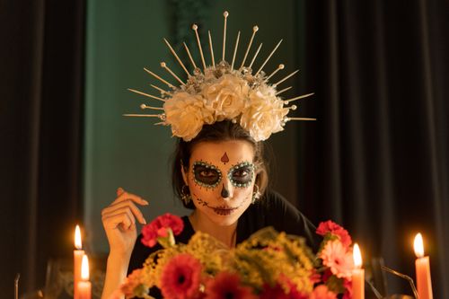 Free An artistic portrait of a woman with Dia de los Muertos makeup and floral crown, surrounded by candles. Stock Photo