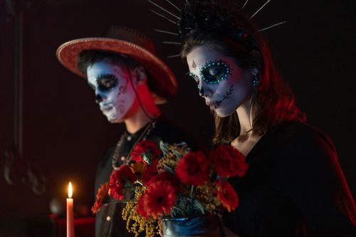 Free Couple celebrating Dia de los Muertos with traditional face paint and flowers in a dark setting. Stock Photo