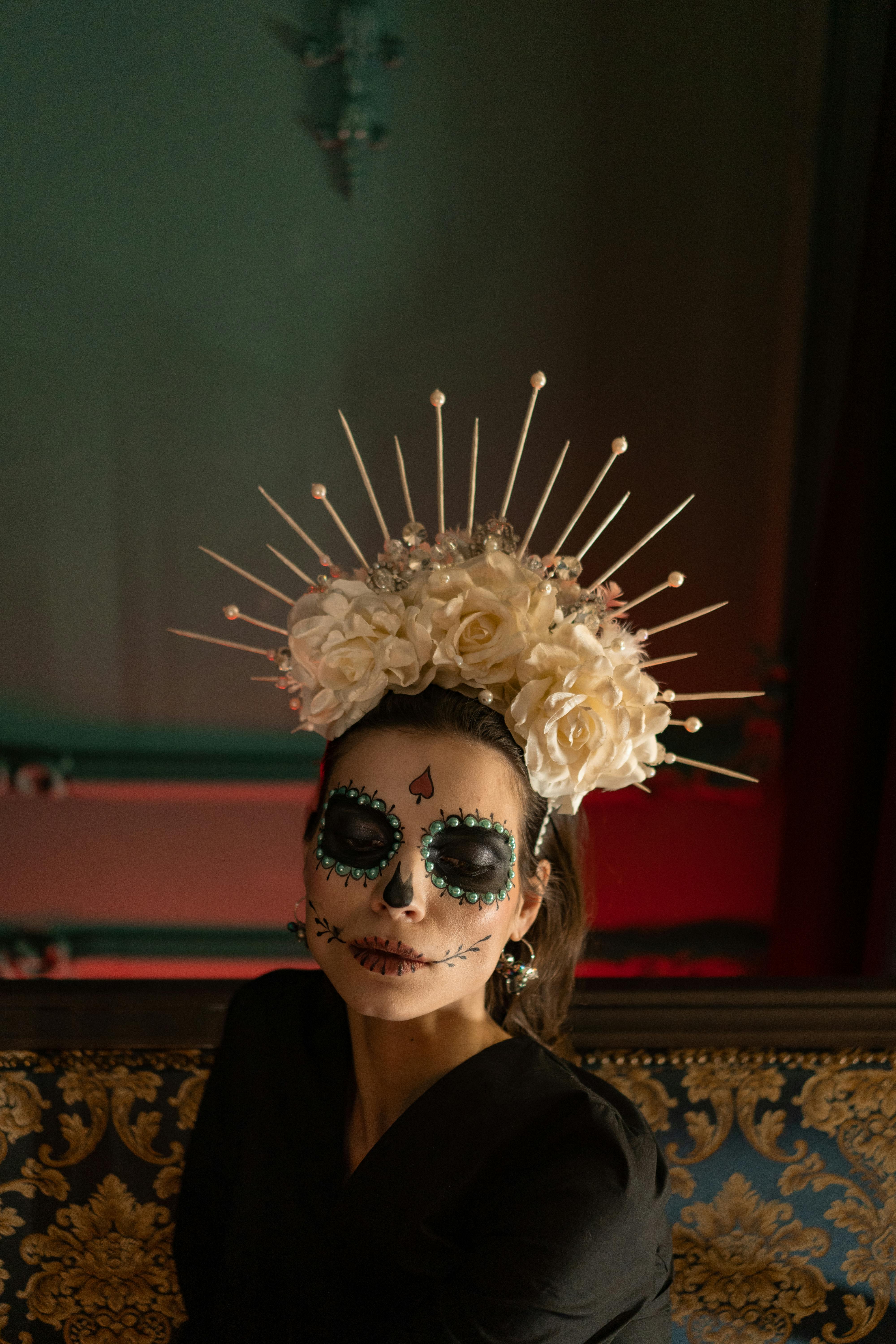A woman in intricate Dia de los Muertos face paint and a floral headdress, captured indoors.