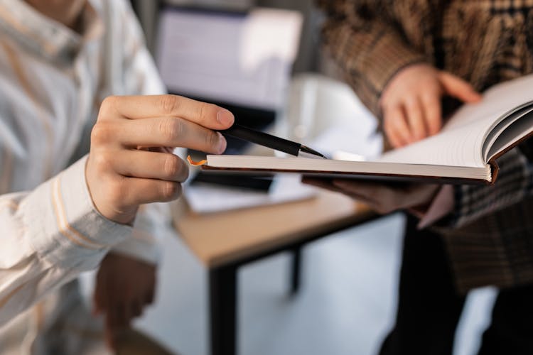 A Person Pointing A Page Of A Book With A Pen