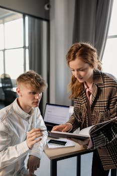 Two young professionals discussing work at a modern office desk.
