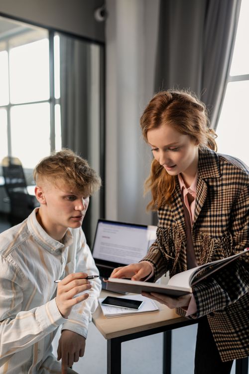 Free Two young professionals discussing work at a modern office desk. Stock Photo
