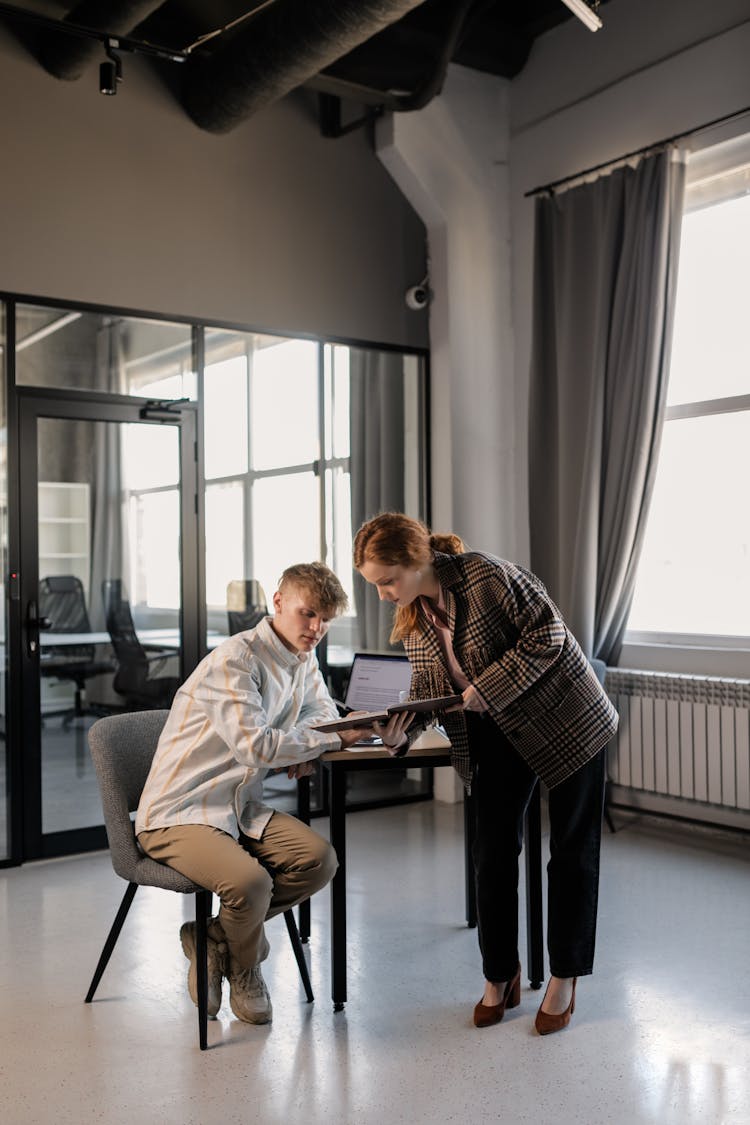 A Woman Standing Beside The Man Sitting On The Chair While Having Conversation