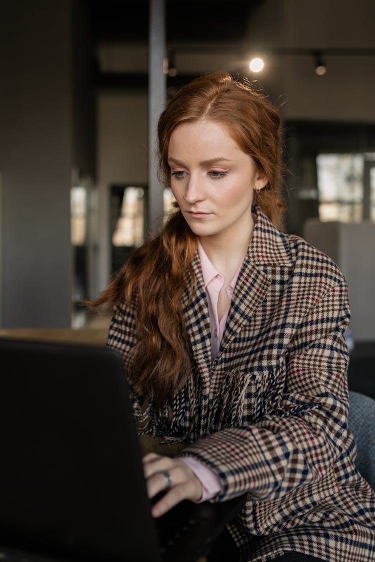 Close-Up Shot Of A Redhead Woman In Checkered Coat Using A Laptop
