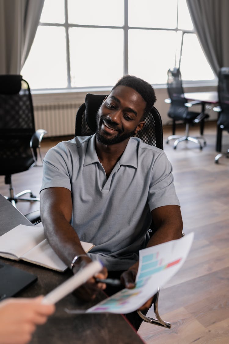 A Bearded Man In A Polo Shirt Holding A Document