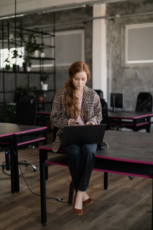 Free A Woman Sitting on a Table while Using Her Gadgets Stock Photo