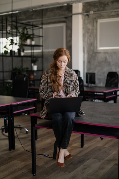 A Woman Sitting on a Table while Using Her Gadgets