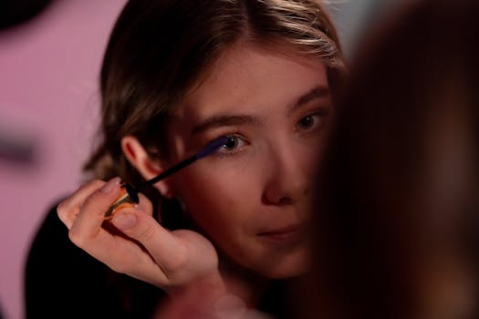 Close-up of a woman applying mascara, focusing intently in a dimly lit setting.