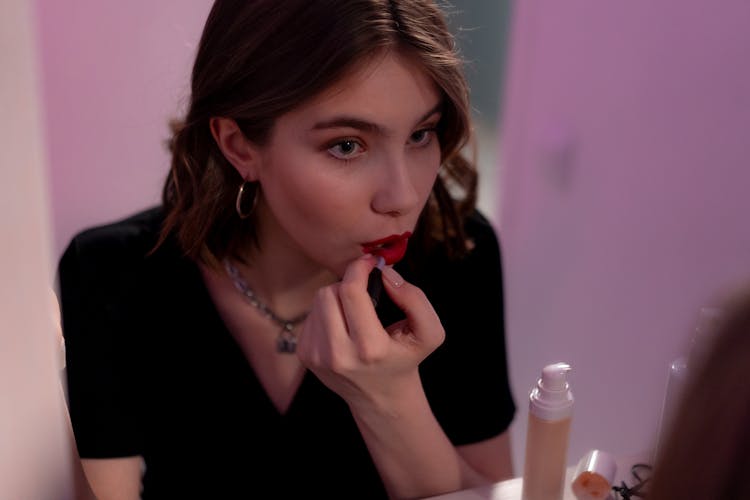 Woman In A Black Top Putting On Red Lipstick On Her Lips