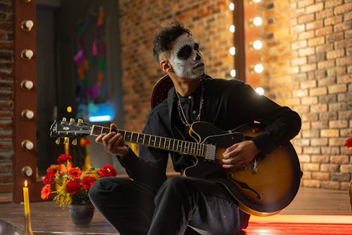 A Man with Face Paint Playing a Guitar
