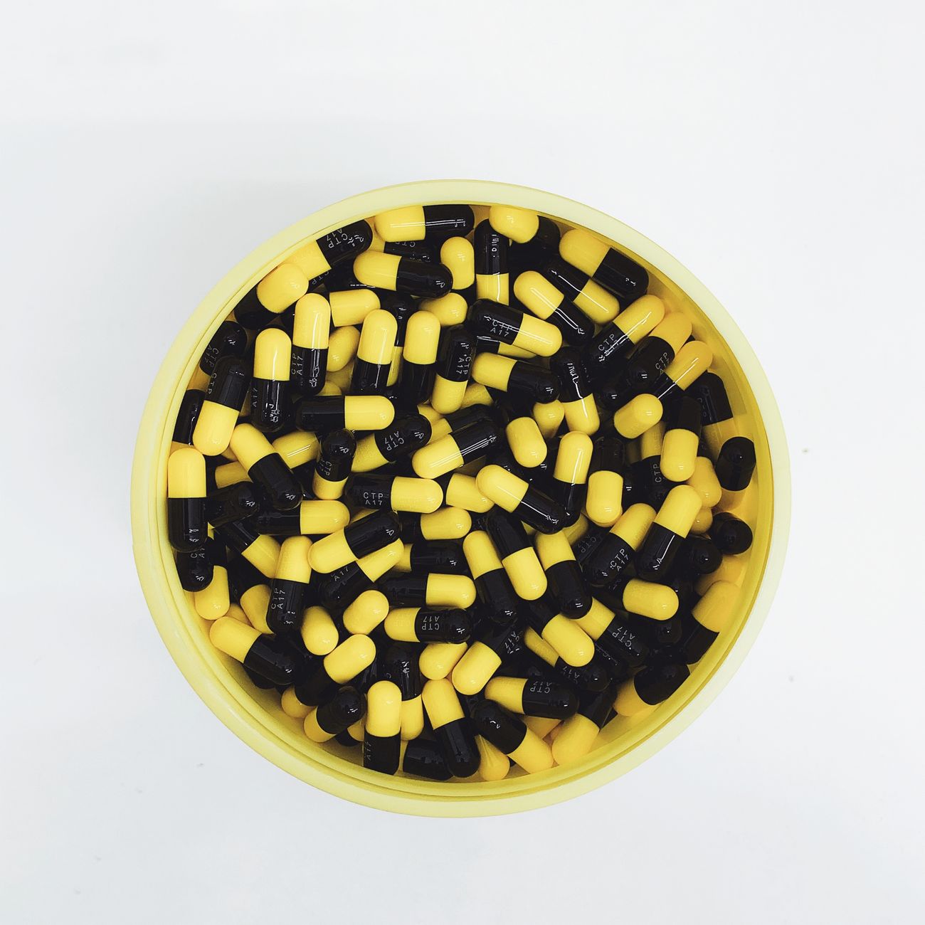Top view of yellow and black capsules in a container, emphasizing pharmaceutical themes.