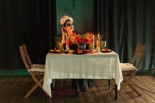 Free Woman in Day of the Dead makeup at candlelit table adorned with flowers and headdress. Stock Photo