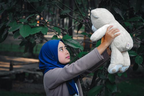 Photo of a Girl with a Blue Hijab Holding a White Plush Toy