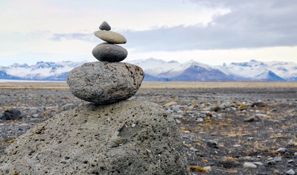 A scenic view of balanced stones against a backdrop of snow-capped mountains in chilly weather.