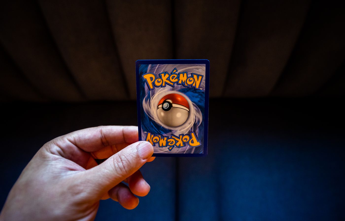 A hand holds a Pokémon trading card with a dark background, emphasizing gaming culture.
