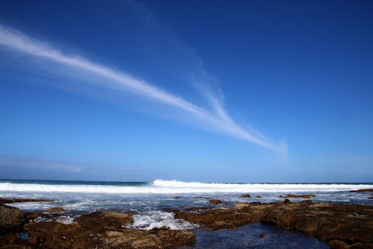 A stunning coastal landscape with waves crashing against rocks under a vivid blue sky.