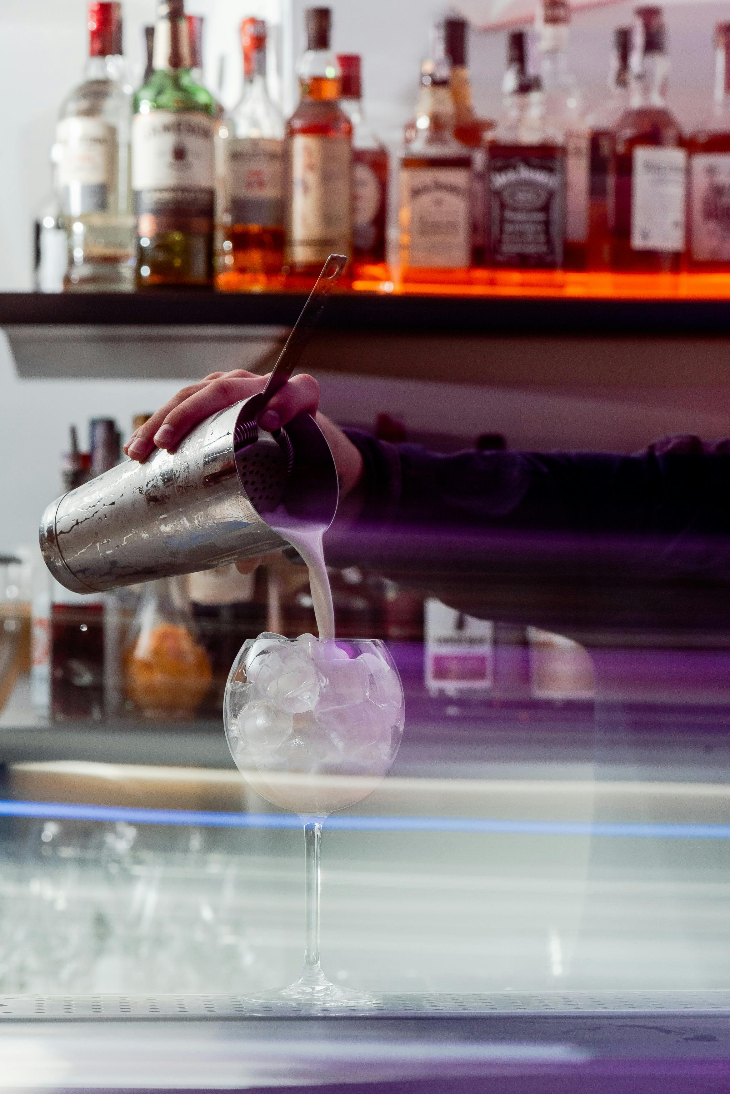 Bartender pours a cocktail into a glass with ice in a vibrant London bar setting, showcasing mixology skills.