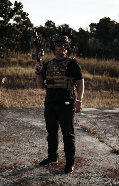 Free A soldier in tactical gear stands confidently outdoors, holding a rifle in a natural setting. Stock Photo