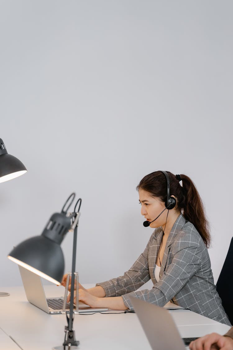 Photo Of A Woman With A Black Headset Typing On Her Laptop