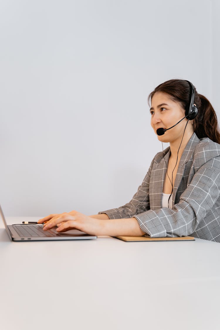 A Woman In White And Gray Plaid Blazer With Black Headset Using A Laptop