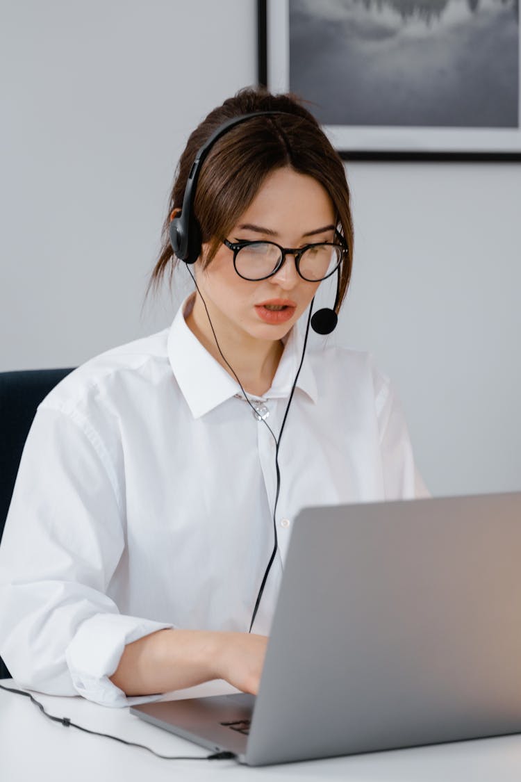 A Woman Talking On A Headset While Using Her Laptop