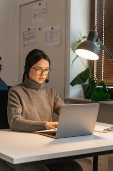 A female call center agent working on a laptop with a headset in an office setting.